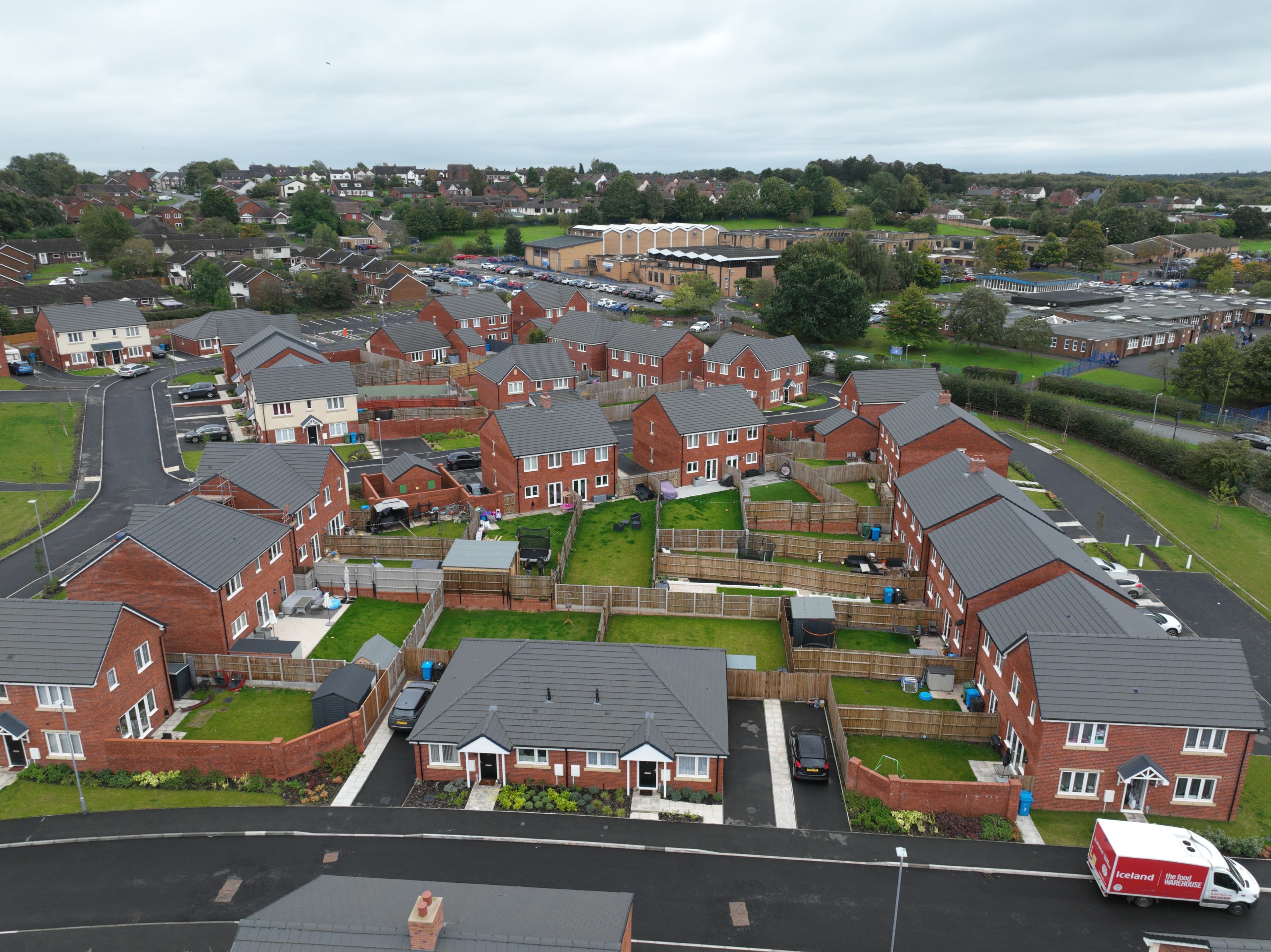 Cheslyn Hay (Saredon Road), Staffordshire: aerial view of the completed scheme, red-brick semi-detached and detached homes with grey pitched roofs arranged around landscaped gardens, surrounding established Staffordshire residential context, Housing Plus / Development Worx affordable scheme.