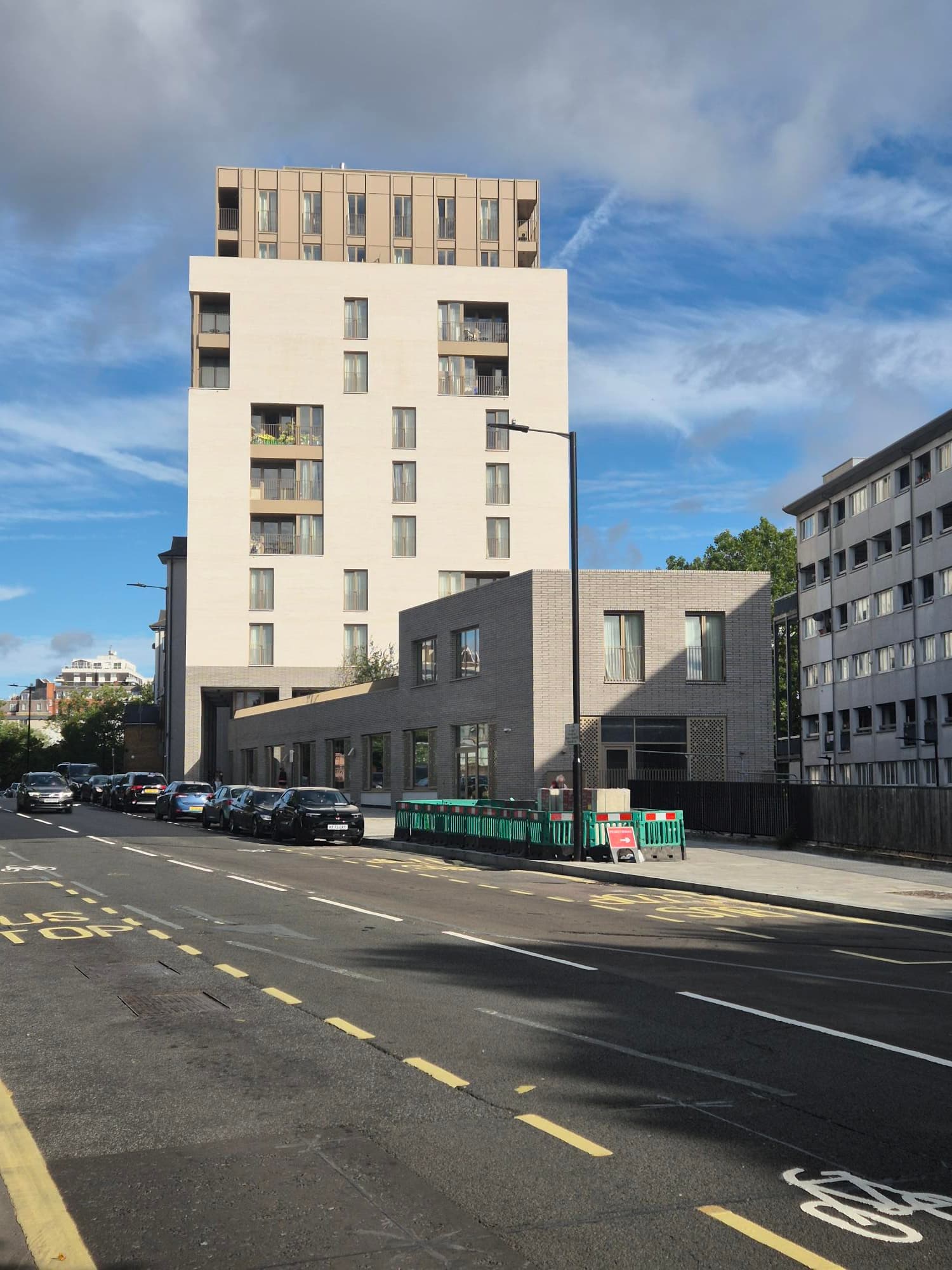 Daventry House (Lisson Arches), Westminster: pale-cream brick block seen from the empty road on a clear summer morning, parked cars in front and the taller darker-brick element of Daventry House behind
