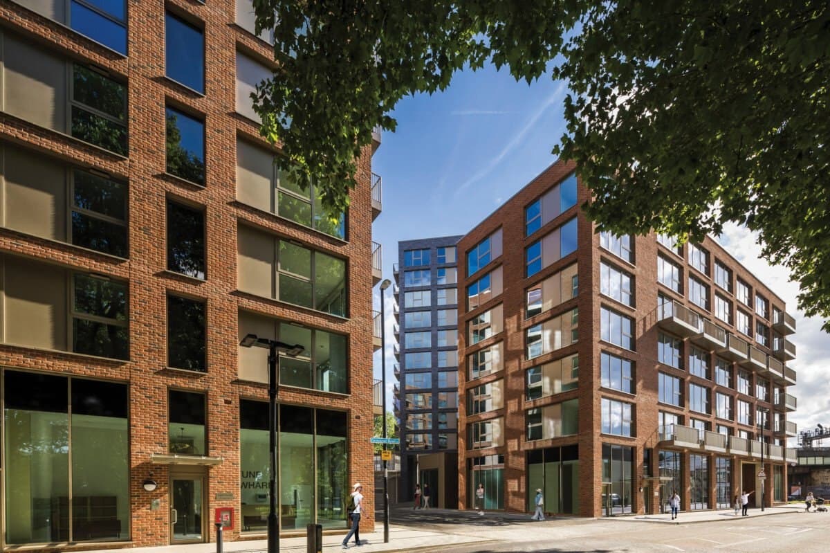 Paynes & Borthwick Wharves, West Greenwich: street-level view of the completed development, modern multi-storey blocks in red and brown brick with full-height glazing and inset balconies under a clear sky, Heritage developer-led private-sale scheme