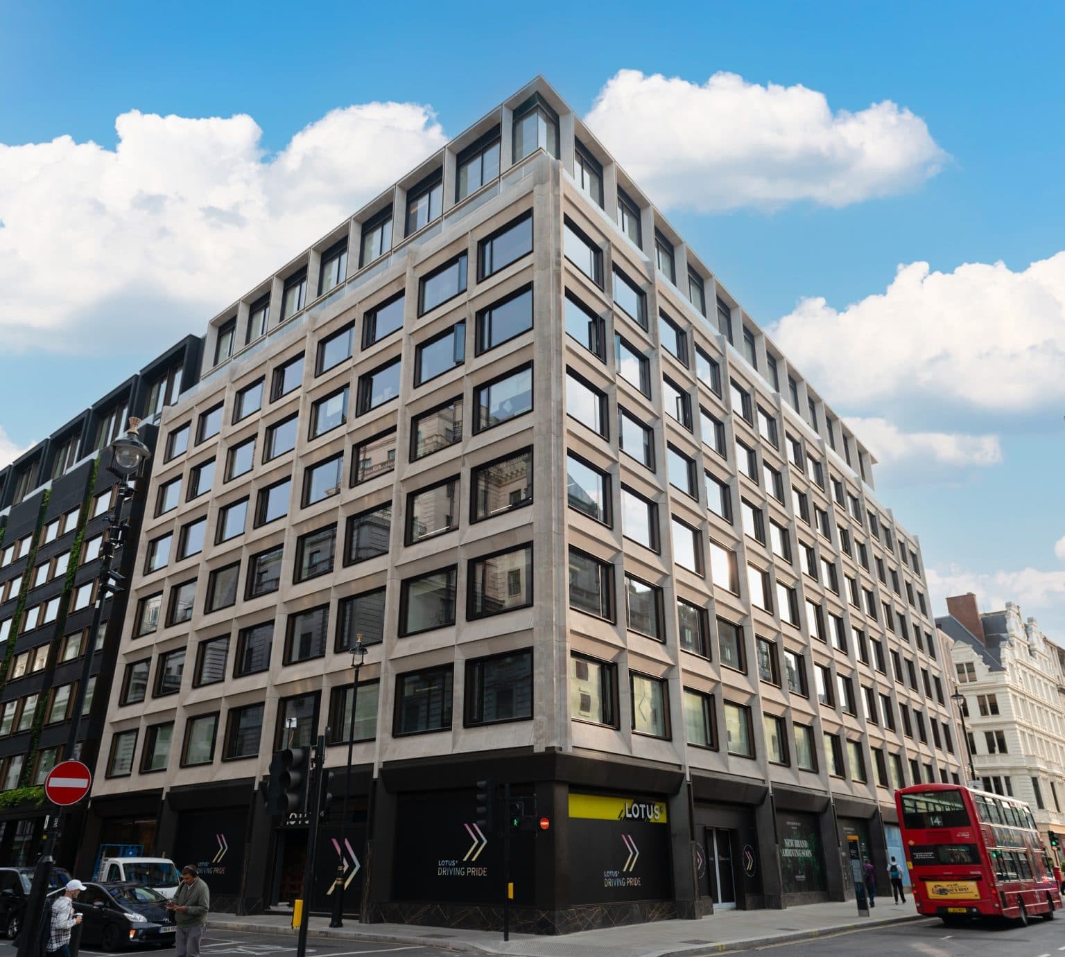 Points Cross Phase 1, Leeds South Bank: a multi-storey mixed-use block in pale Portland-stone-style cladding, regular window grid wrapping the corner, ground-floor retail frontage with active signage, street scene at pedestrian level beneath a clear sky.