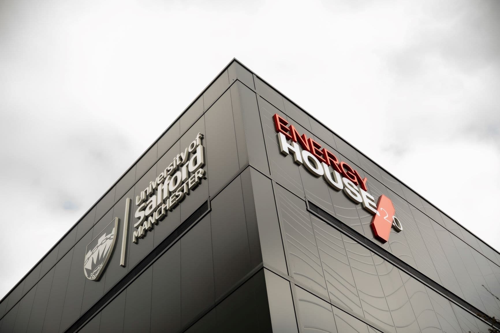 RAMMIC, Energy House, Salford: the corner of the black-clad Energy House 2.0 building at the University of Salford, with the Energy House and University of Salford branding on the facade against a grey sky, University of Salford (Energy House Labs) scheme