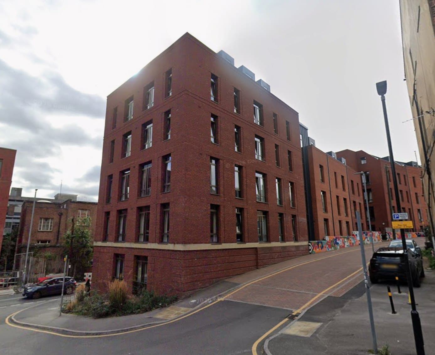 St Johns House, Leeds: red-brick apartment block of five storeys with regular windows curving along the city-centre street with a cycle lane, Leeds and Yorkshire Housing scheme