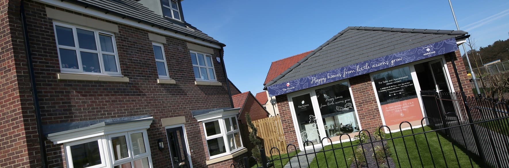 The Acorns, Spennymoor: completed red-brick three-storey homes alongside the marketing suite with the 'Happy homes from little acorns grow' fascia sign — Tarras Park Properties affordable scheme in County Durham.