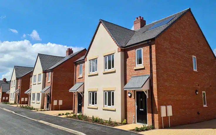 Annfield Plain, County Durham: completed terrace of red-brick and cream-rendered two-storey homes with grey pitched roofs, pitched porch hoods and roof-mounted PV, Karbon Homes affordable scheme