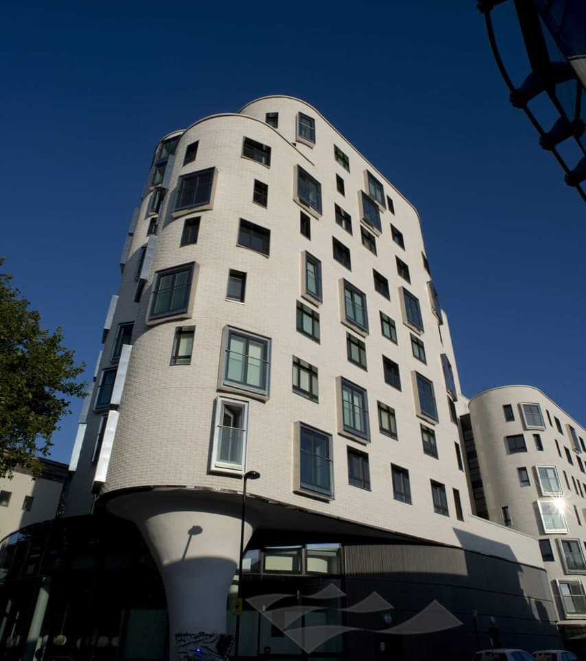 Clapham One, Lambeth SW4: completed mixed-tenure scheme with curved white-brick façade, deep-set window reveals and sculpted ground-floor column, viewed against a deep blue sky