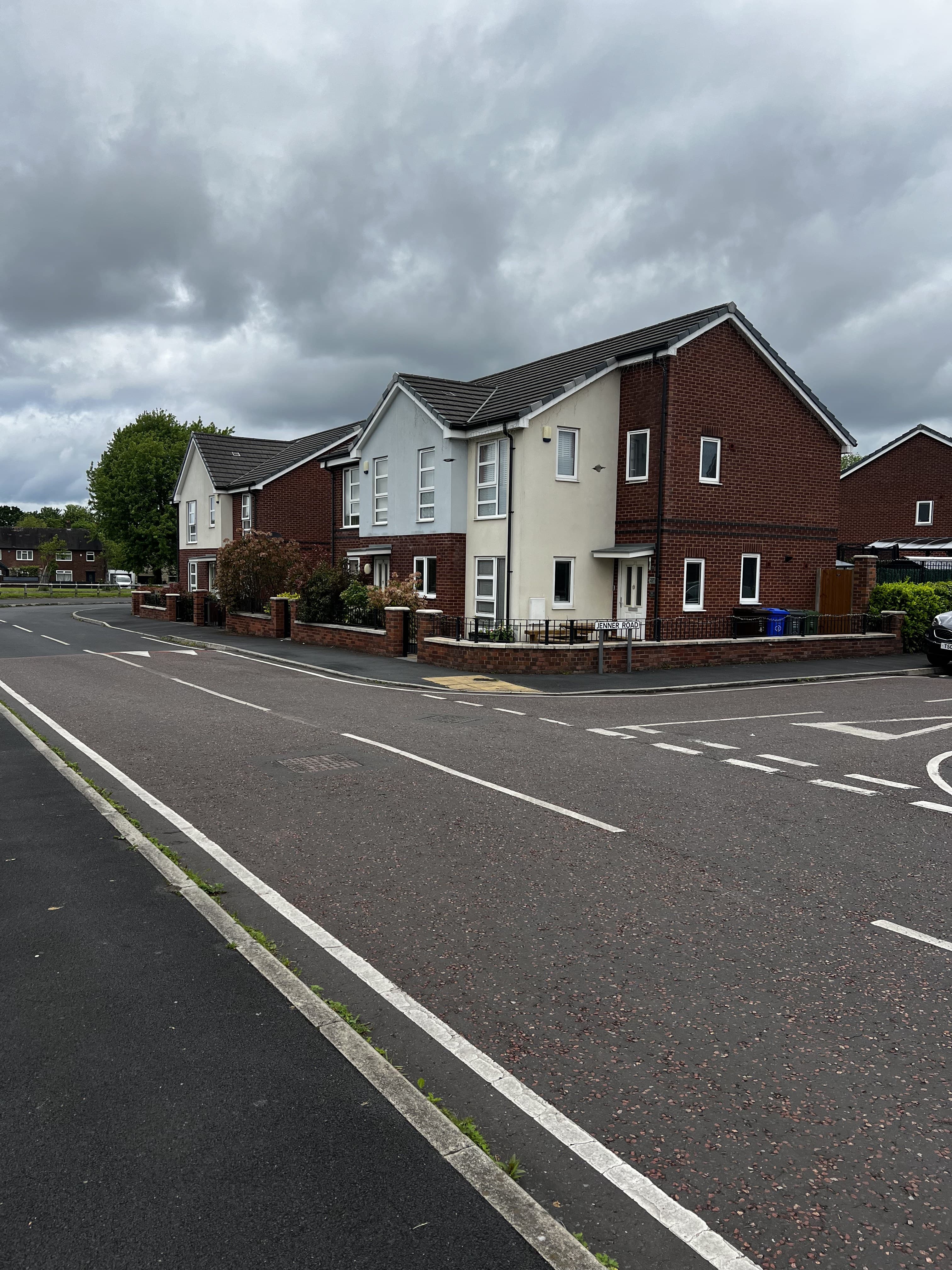 Cotefield Road, Wythenshawe: corner view of a detached three-storey block with white-rendered upper floors and red-brick base, pitched grey roof and fenced front gardens, viewed across a junction.