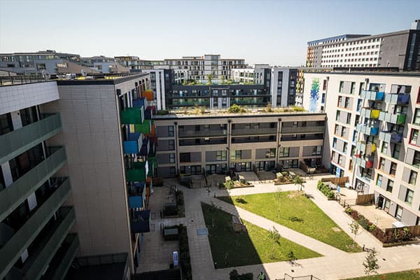 Hale Village, Tottenham (N17): aerial view of a residents' courtyard with grass and footpaths, ringed by mid-rise blocks in green and yellow grid-balcony cladding, part of the 1,226-home Tottenham Hale regeneration masterplan