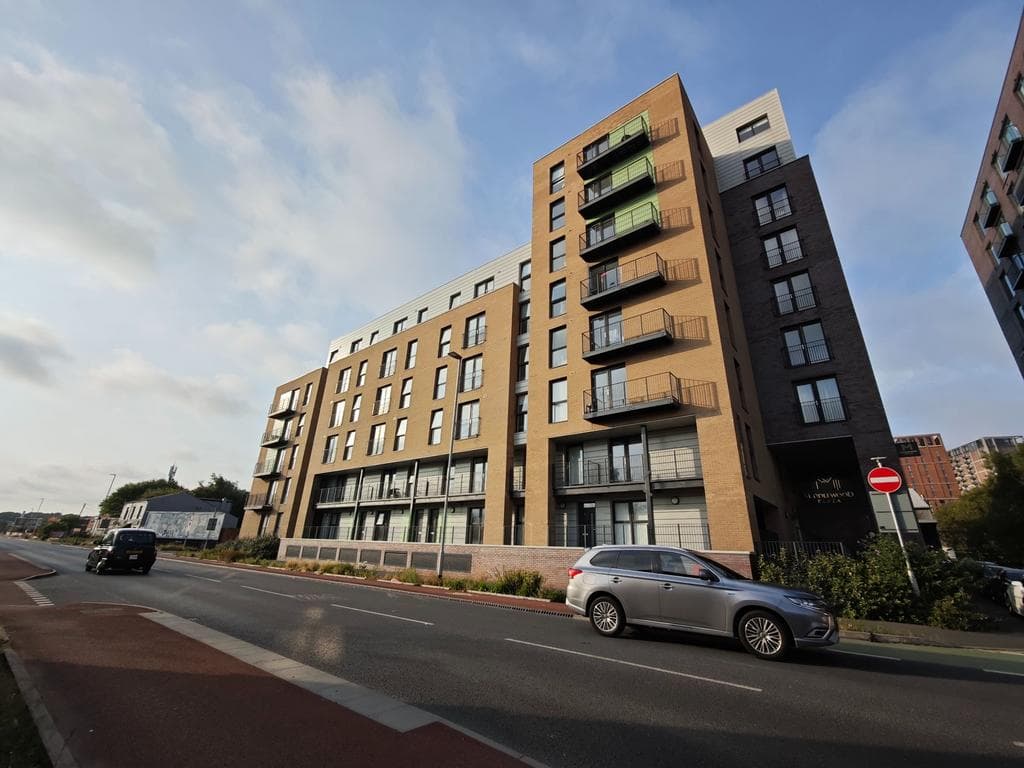 Middlewood Plaza, Liverpool Street, Salford: completed seven-storey BTR block in tan brick with anthracite-clad vertical balcony columns and "Linkwood Plaza" entrance, viewed from a wide road with cycle lane, Rodus / UL + High Street Group JV