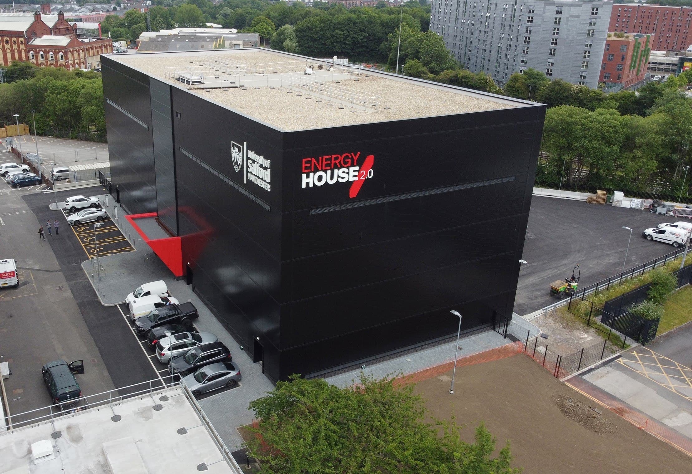 RAMMIC, Energy House, Salford: aerial view of the black-clad Energy House 2.0 research building at the University of Salford, with its environmental test chambers, car park and surrounding streets, University of Salford (Energy House Labs) scheme