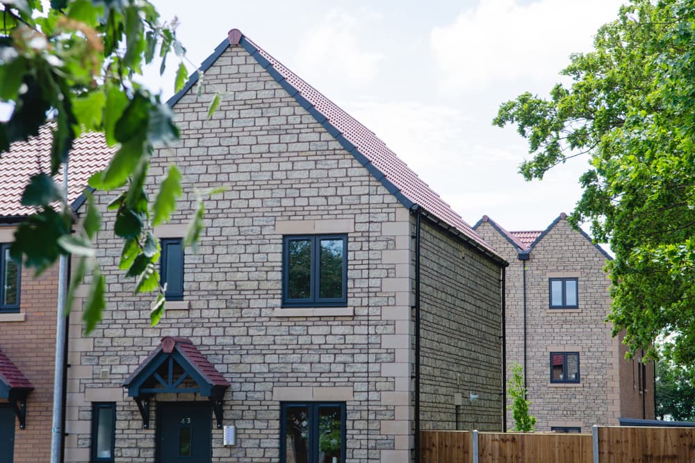 The Moorings, Pucklechurch: completed Cotswold-stone semi-detached pair with red-tile pitched roof, dark window surrounds and timber-trimmed porch, LiveWest affordable scheme