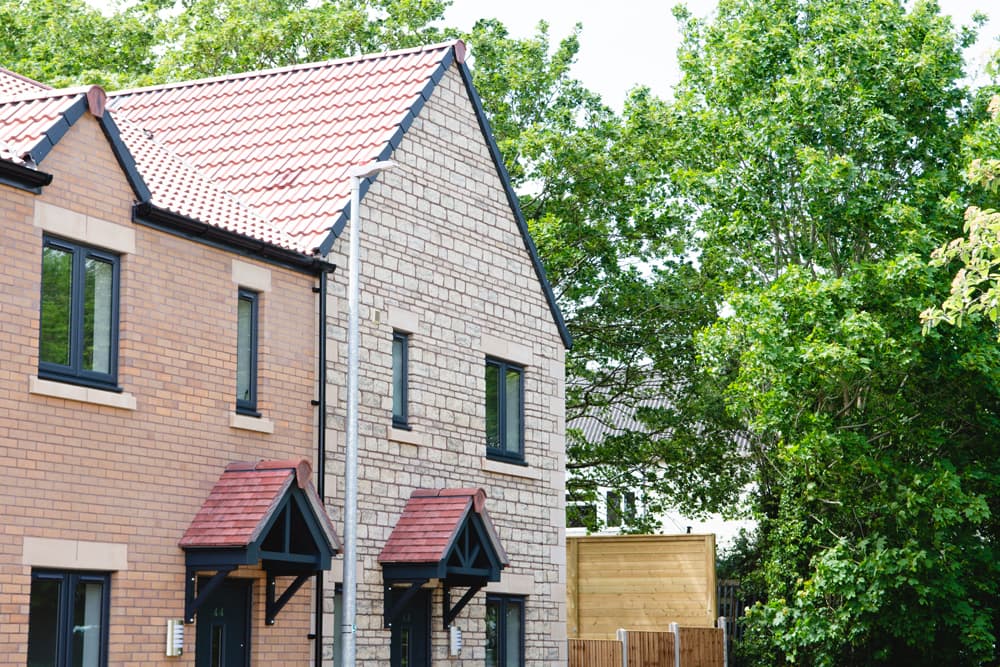 The Moorings, Pucklechurch: terrace end of brick and Cotswold-stone homes with red-tile pitched roofs and pitched porch hoods over each front door