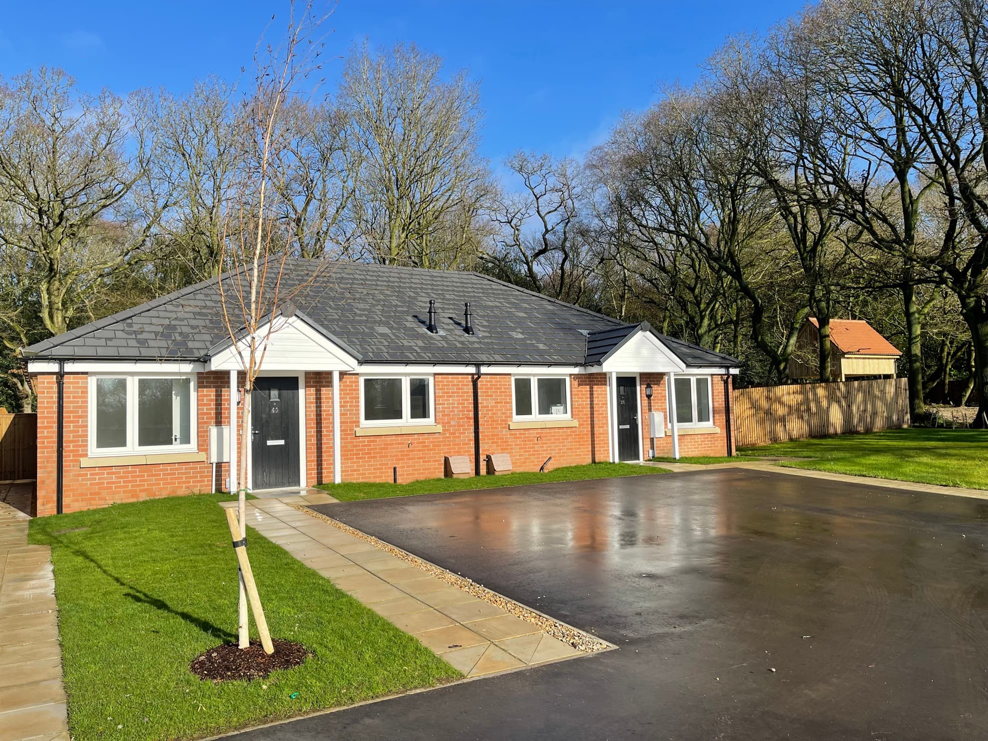 Tower Mill, Necton: completed pair of single-storey bungalows in red brick with grey pitched roofs, newly-laid driveways and a young tree on the lawn